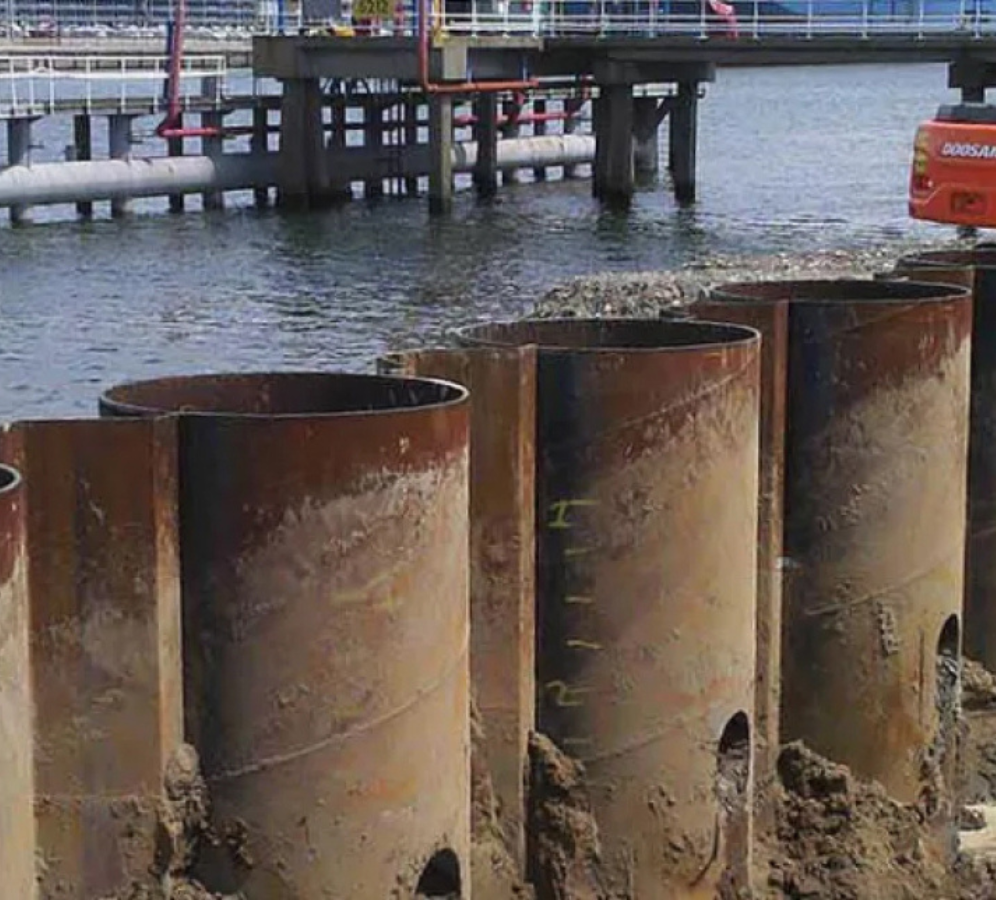 Completed combi wall system with interlocked regular sheet piles between steel pipe piles along a waterfront construction site