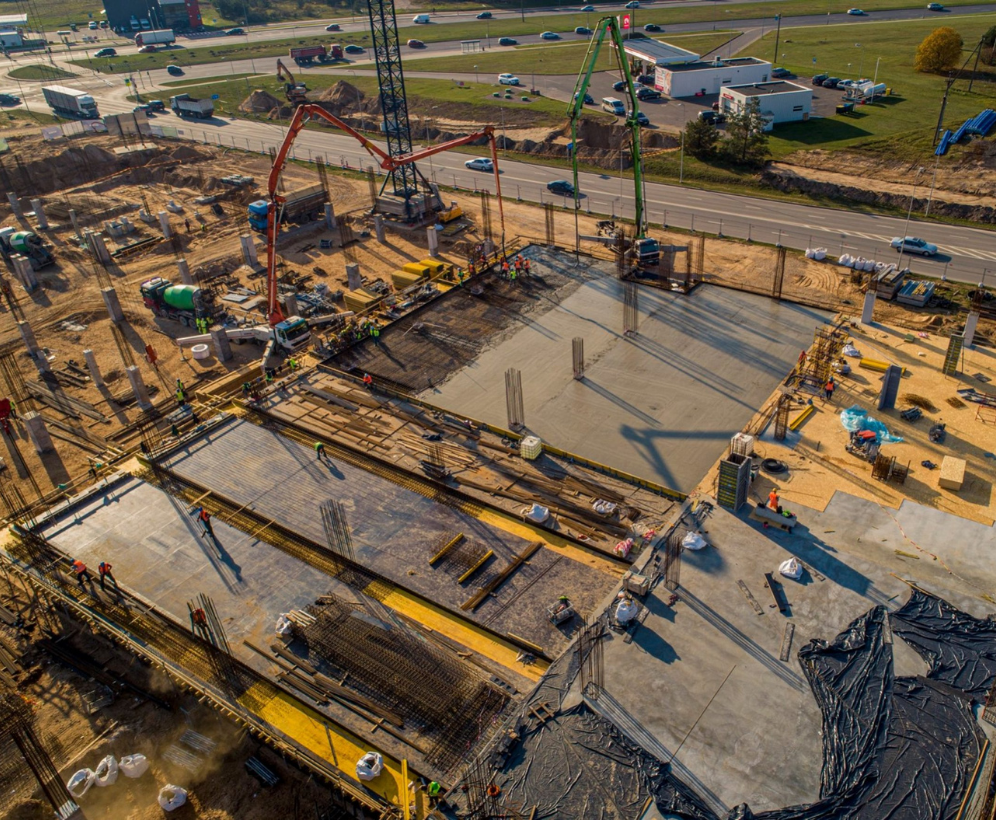 Betonieren auf der Baustelle Luftaufnahme einer Großbaustelle, auf der die Vorspannbetontechnologie angewendet wird, während des Betonierens mit sichtbarer Schalung, Bewehrung und Pumpenfahrzeugen in der Nähe einer Hauptstraße