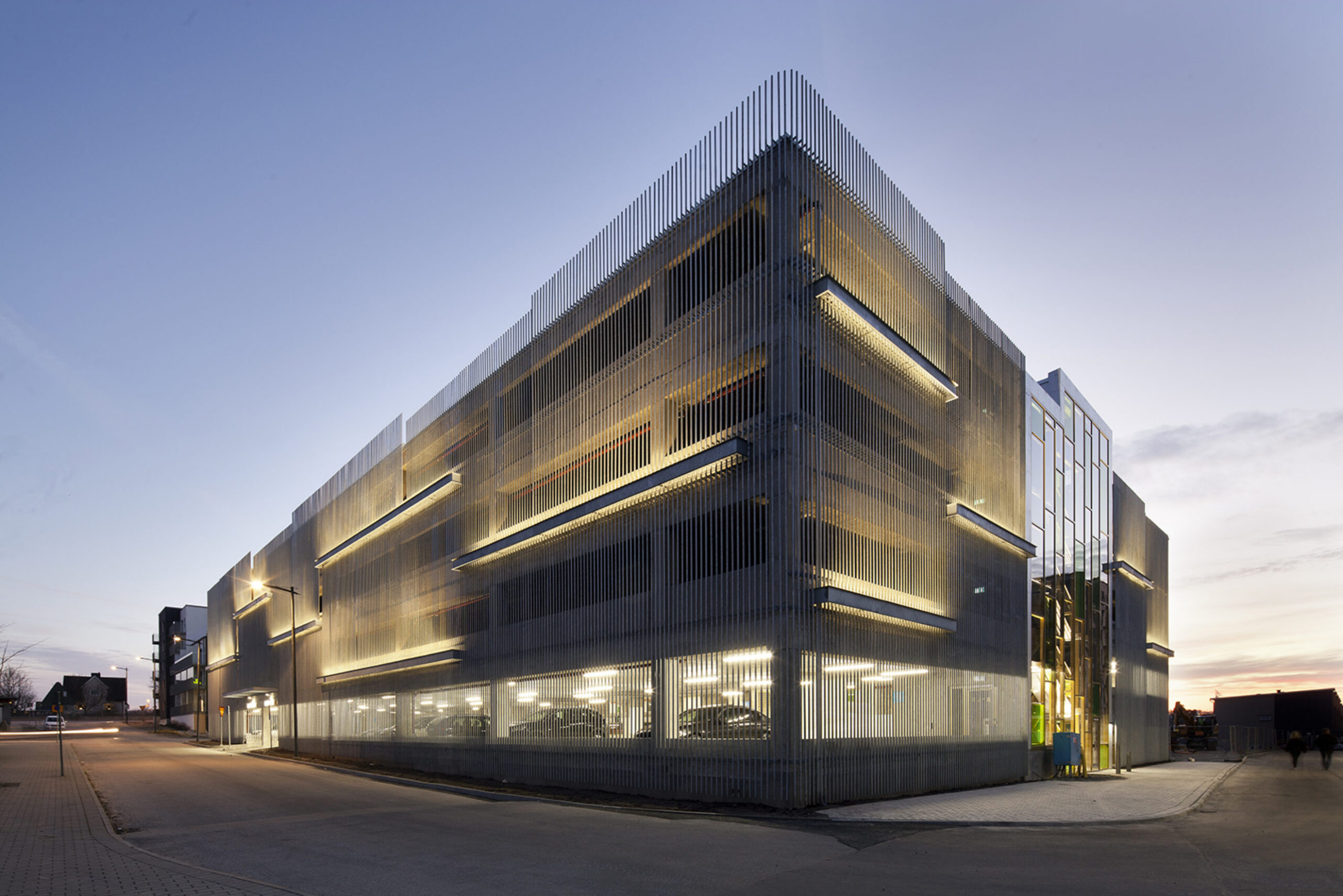 Modernes mehrstöckiges Parkhaus Modernes mehrstöckiges Parkhaus mit angewandter Post-Tension-Betontechnologie und beleuchteten Fassadenpaneelen in der Abenddämmerung, das architektonisches Stahl- und Glasdesign präsentiert.