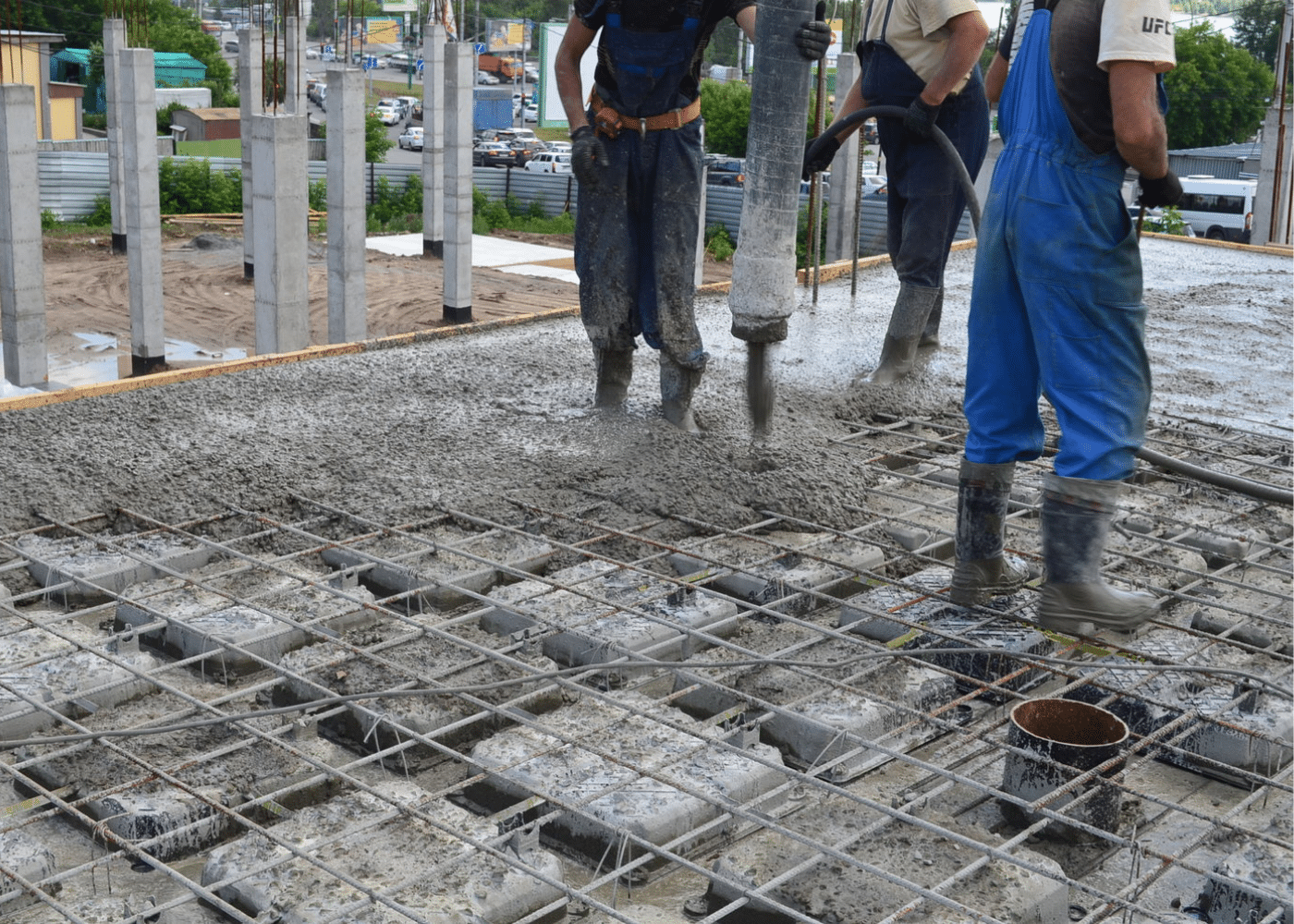 Workers performing the second-stage concrete pouring over void formers and rebar mesh to complete the structural slab.
