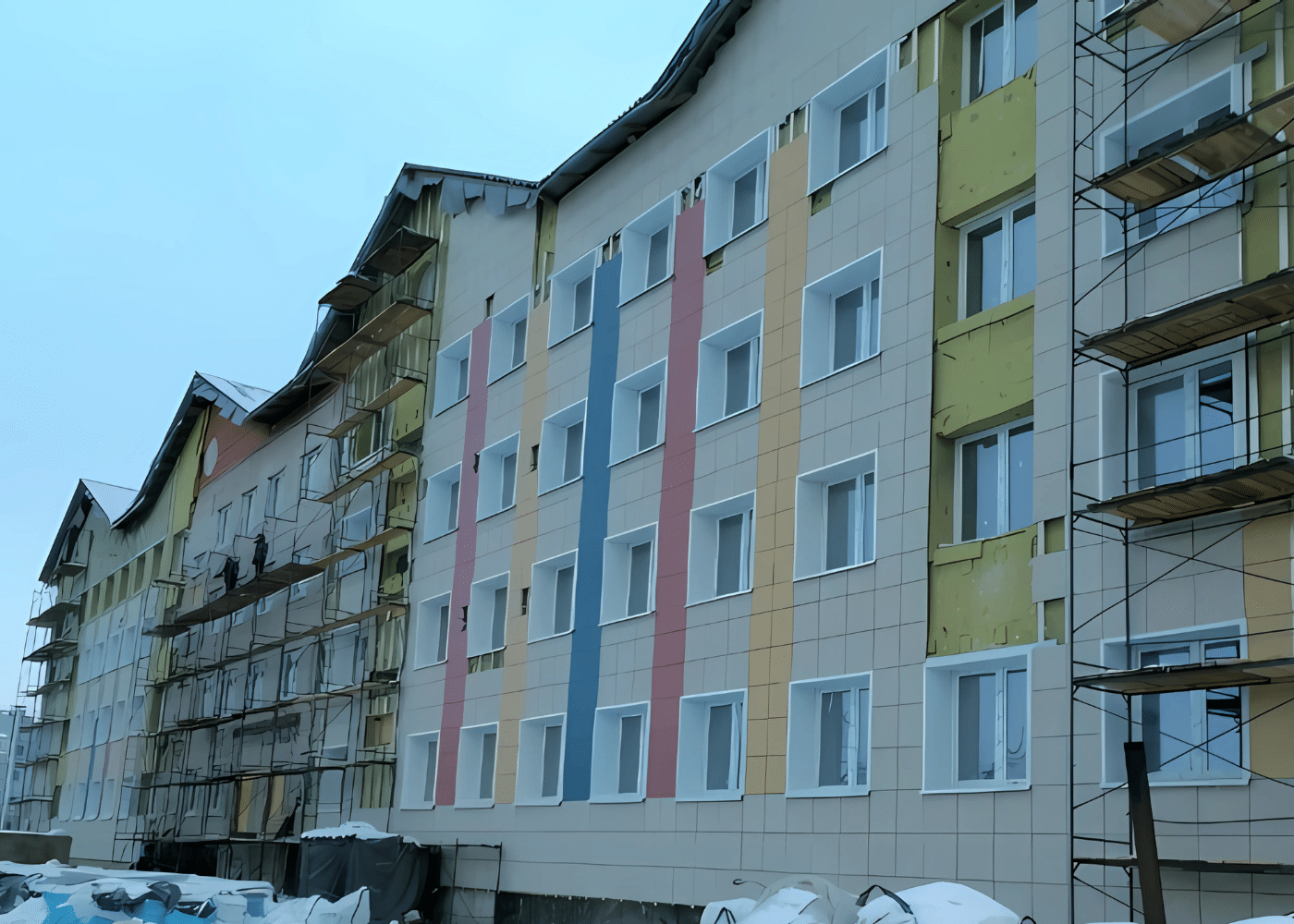 Ongoing renovation of a mid-rise residential building with scaffolding and newly installed colorful facade panels.