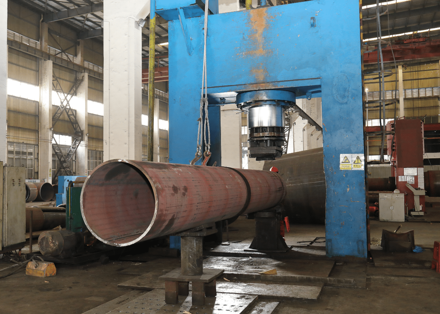 Straight-seam welded steel pipe under hydraulic press during the LSAW production process.