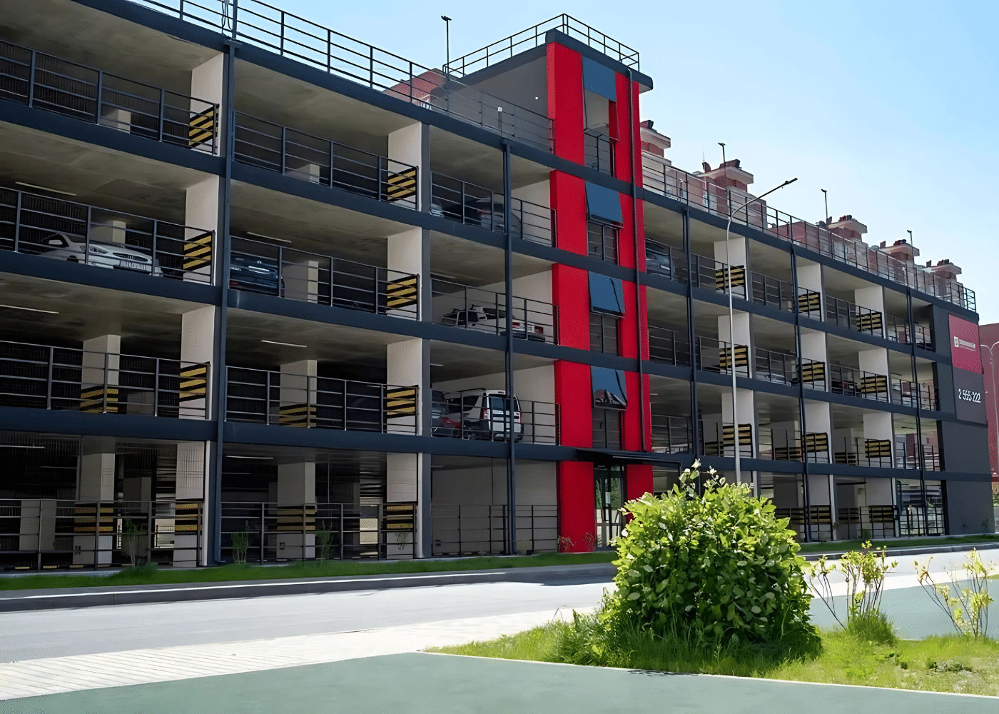 Multi-level elevated parking garage with reinforced concrete floors, open façade, and a red vertical core for stair and elevator access.