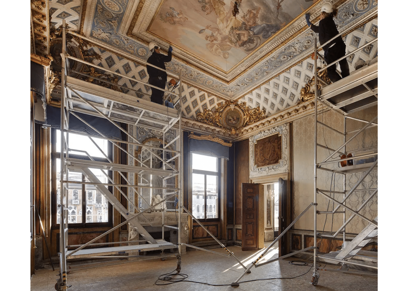 Two workers using aluminium scaffolding towers for detailed ceiling painting and restoration inside a historic building, demonstrating stable platforms that support precise work at height with maximum safety.
