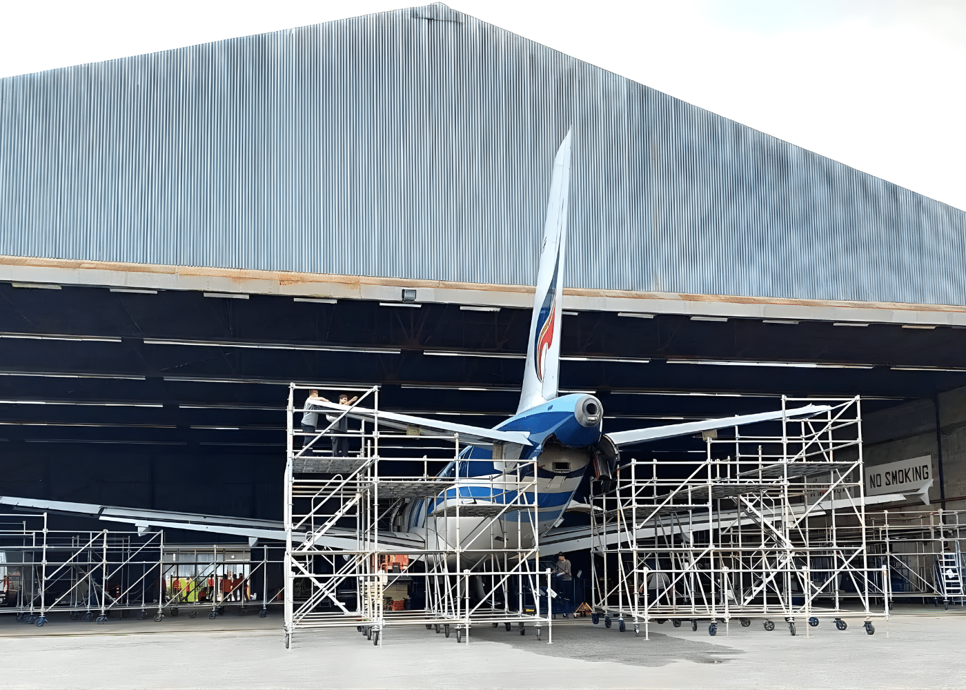 Aircraft maintenance hangar with multiple scaffolding towers surrounding an aeroplane, providing covered and reliable access for inspection and repair operations in industrial environments.